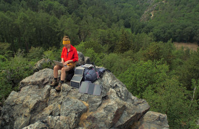 Hiker using laptop while sitting on rocky mountain
