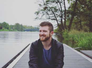 Portrait of smiling man standing by river against sky