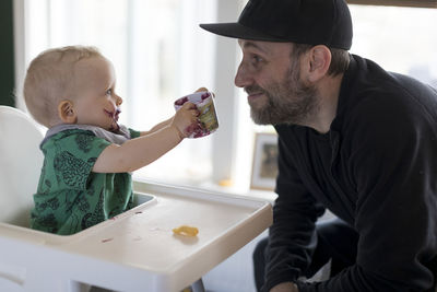 Father supervising son eating in high chair