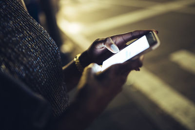 Hands of woman holding smartphone at night, close-up