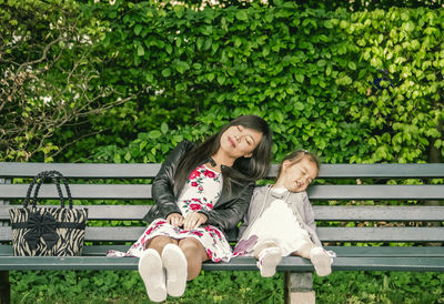 Full length of happy woman sitting on bench in park