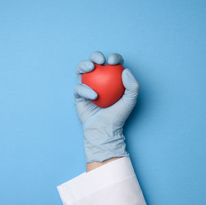 Female hand in blue latex gloves holding a red heart, donation concept, top view