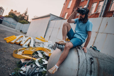 Man with vr goggles sitting on cylinder on street