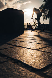 Silhouette of man on a bmx on street against sky during sunset