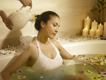 Cropped hand of person pouring milk on woman in bathtub