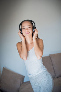 Portrait of smiling young woman using phone while standing on sofa at home