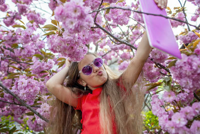 Portrait of young woman wearing sunglasses standing against tree