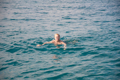 Active laughing young woman enjoying swimming in refreshing clear sea water on sunny day, vacation