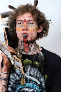 Man with face paint holding guitar against wall at home