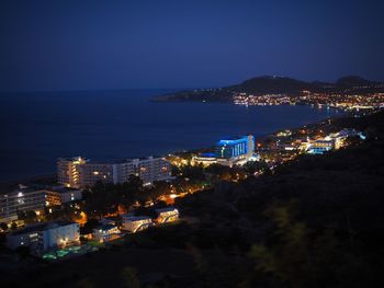 High angle view of illuminated city by sea against sky at night