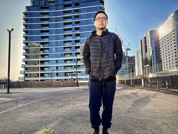 Young asian man standing against buildings, construction crane and sky.