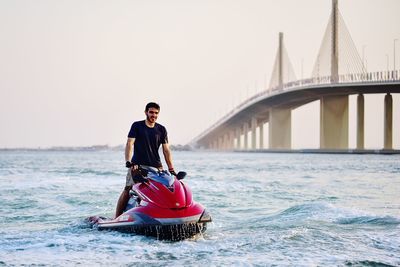 Man riding motorcycle on bridge over sea against sky