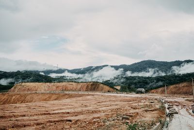 Dirt road with small house with foggy mountain behind