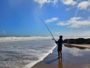 Full length of man fishing at beach against sky