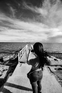 Rear view of woman standing at beach against sky