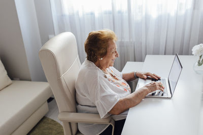 Smiling senior woman using laptop sitting at table