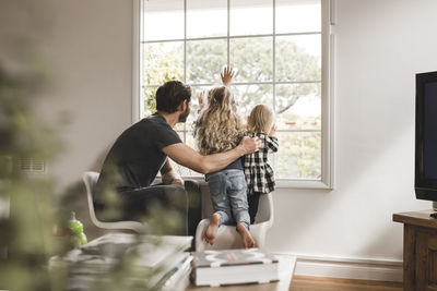 Rear view of people standing against window at home