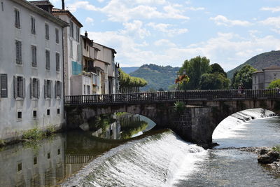 Arch bridge over river amidst buildings against sky