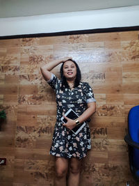 Portrait of a smiling young woman standing against wall