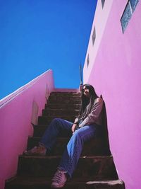 Low angle view of woman sitting against building against clear sky