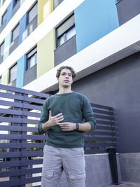 Low angle of man in green sweater and pants with brown hair standing against contemporary building