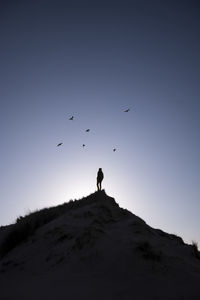 Low angle view of silhouette men standing on mountain against clear sky