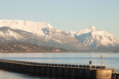 Man standing on pier over sea against snowcapped mountains