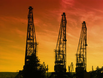 Silhouettes of giant cranes at the port of transhipment against a bloody sunset sky