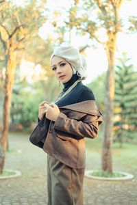 Portrait of young woman wearing hat standing against trees