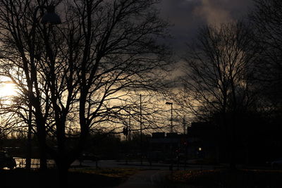 Silhouette bare trees by street against sky at sunset