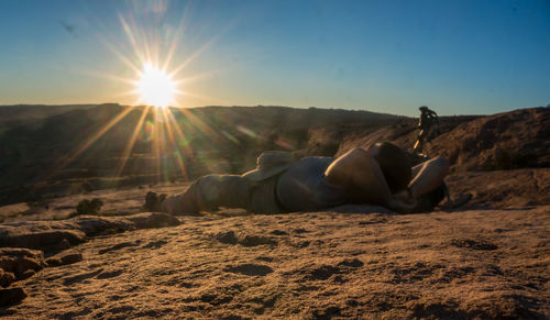 Man lying on land against sky during sunset