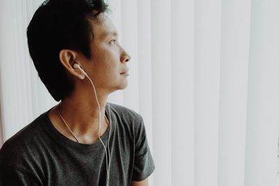 Close-up of man listening to music against white blinds