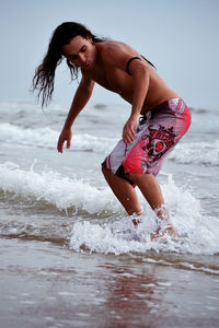 Shirtless young man on surfboard at sea shore