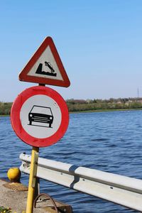 Road sign by river against clear sky