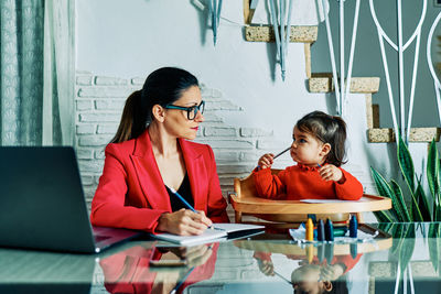 Young executive woman working from home while taking care of her young daughter