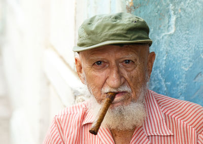 Portrait of senior man wearing cap smoking cigar while sitting outdoors