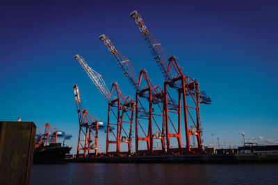 Cranes at commercial dock against clear blue sky