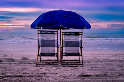 Two beach chairs and umbrella on the beach at dusk