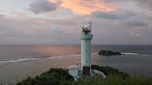 Lighthouse by sea against sky during sunset