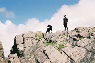 Woman with dog standing on rock against sky