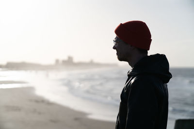 Side view of man standing at beach against sky