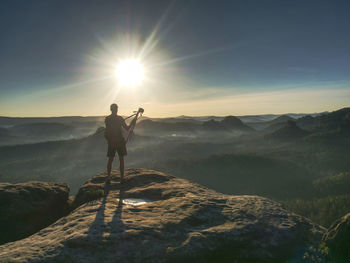 Man photographer taking photo on sunset mountain peak. hiker in shorts and backpack on sweaty bag