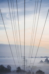 Low angle view of electricity pylon against sky during foggy weather