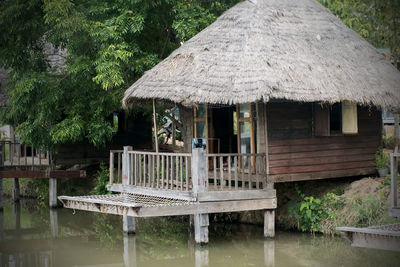 Wooden house beside the water, thatched with grass, with trees beside, sitting beside the river