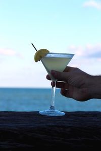 Close-up of hand holding drink against sea