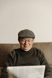 Senior man reading newspaper while siting on sofa at home