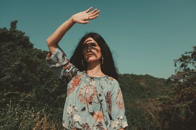 Young woman standing by tree on field against sky