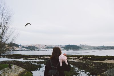 Rear view of woman photographing at beach against sky