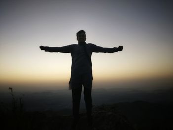 Man with arms outstretched standing against sky during sunset