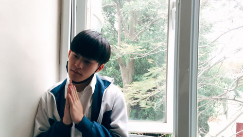 Young man looking through window at home